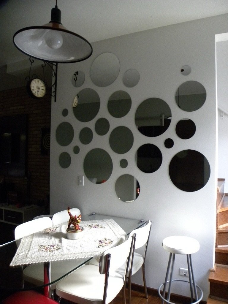 Collection of various sized round frameless mirrors arranged like bubbles on a white dining room wall behind a glass table.